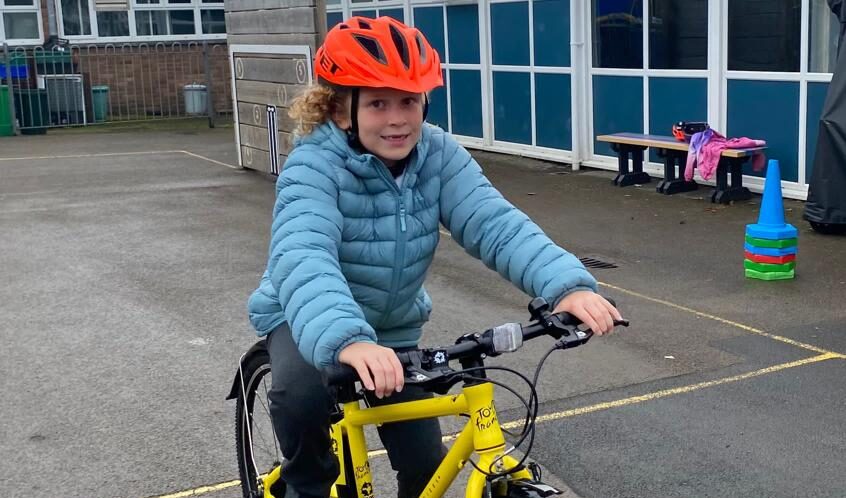 A girl is riding a yellow bike. She wears a blue coat and a red helmet.